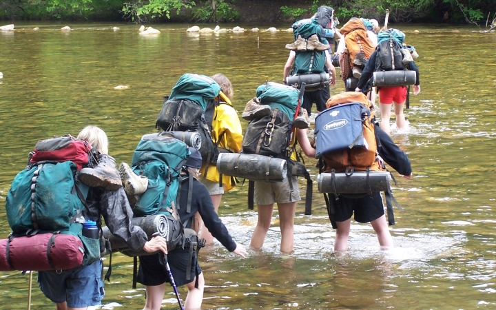 A group of students wearing backpacks make their way through ankle-deep water.